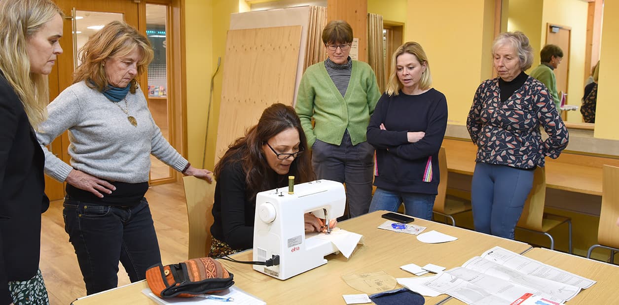Adult Education students standing around someone on a sewing machine