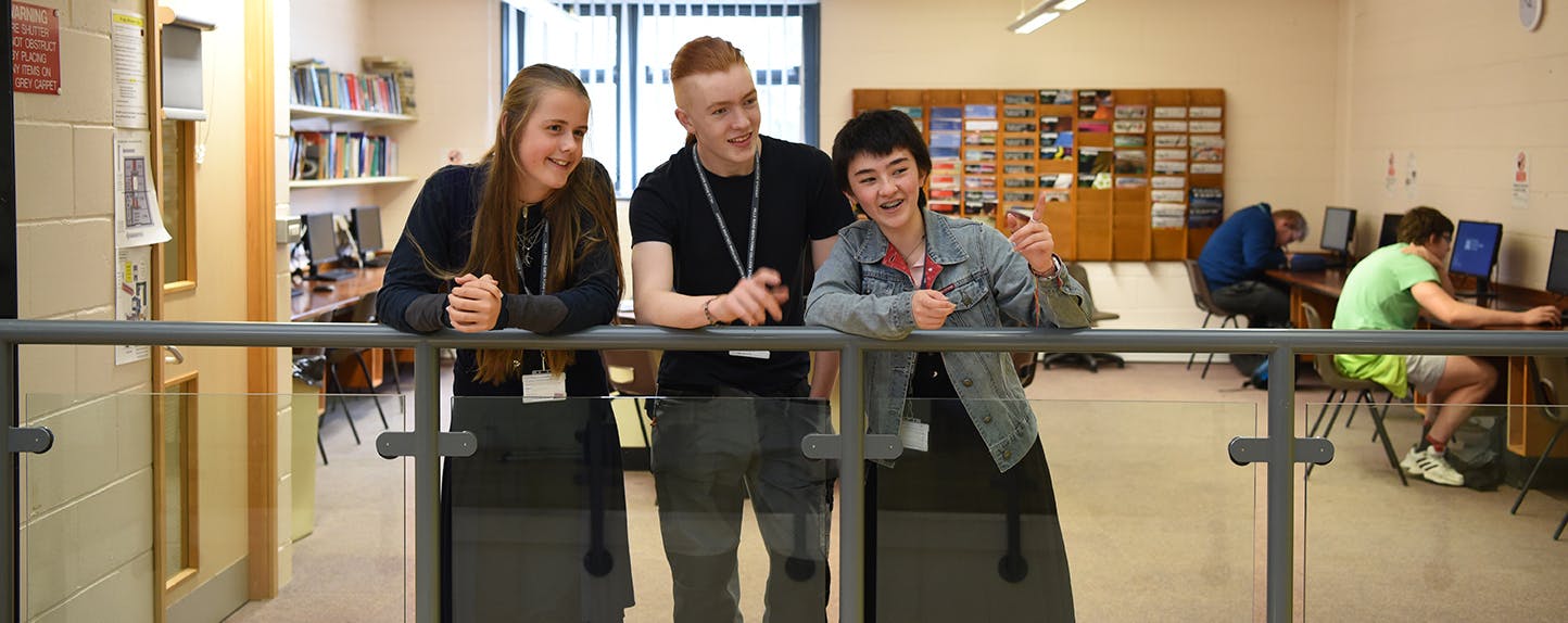 three students standing against glass wall
