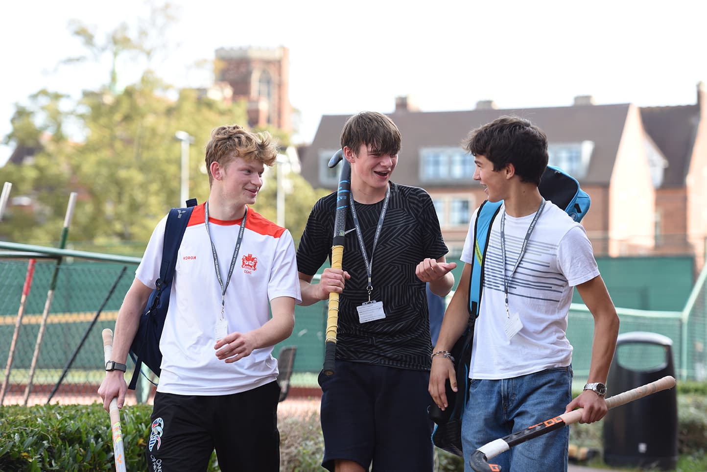 three students walking together holding hockey sticks